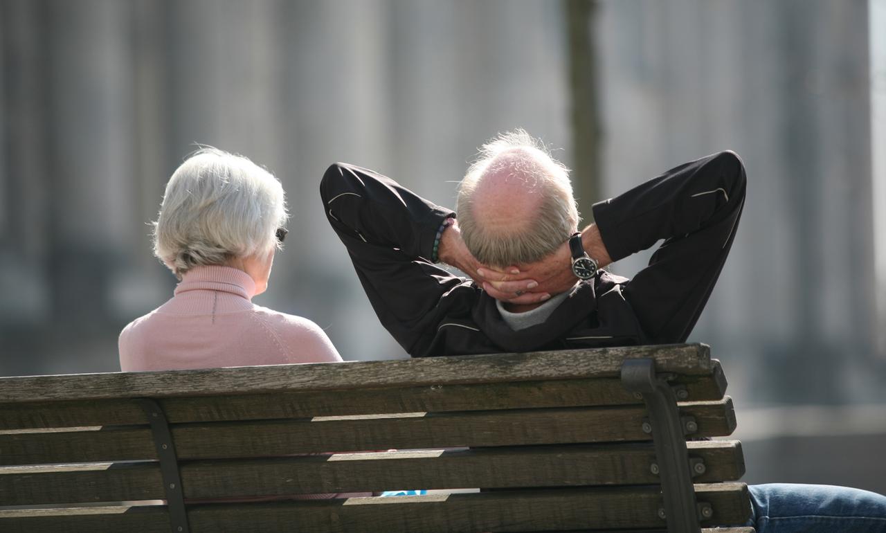 Ein Rentnerpaar genießt die Sonne vor dem Parlament.