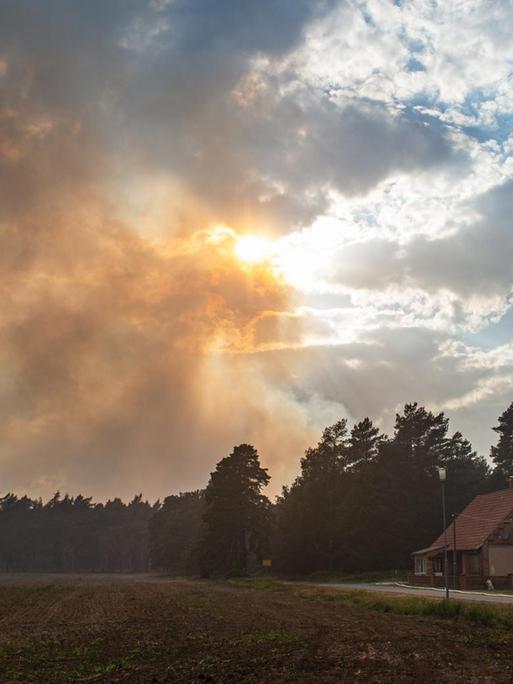 In Mecklenburg-Vorpommern, Hohen Woos, schützen Feuerwehrleute Häuser, deren Bewohner das Gebiet verlassen mussten, während Rauch in den Abendhimmel steigt