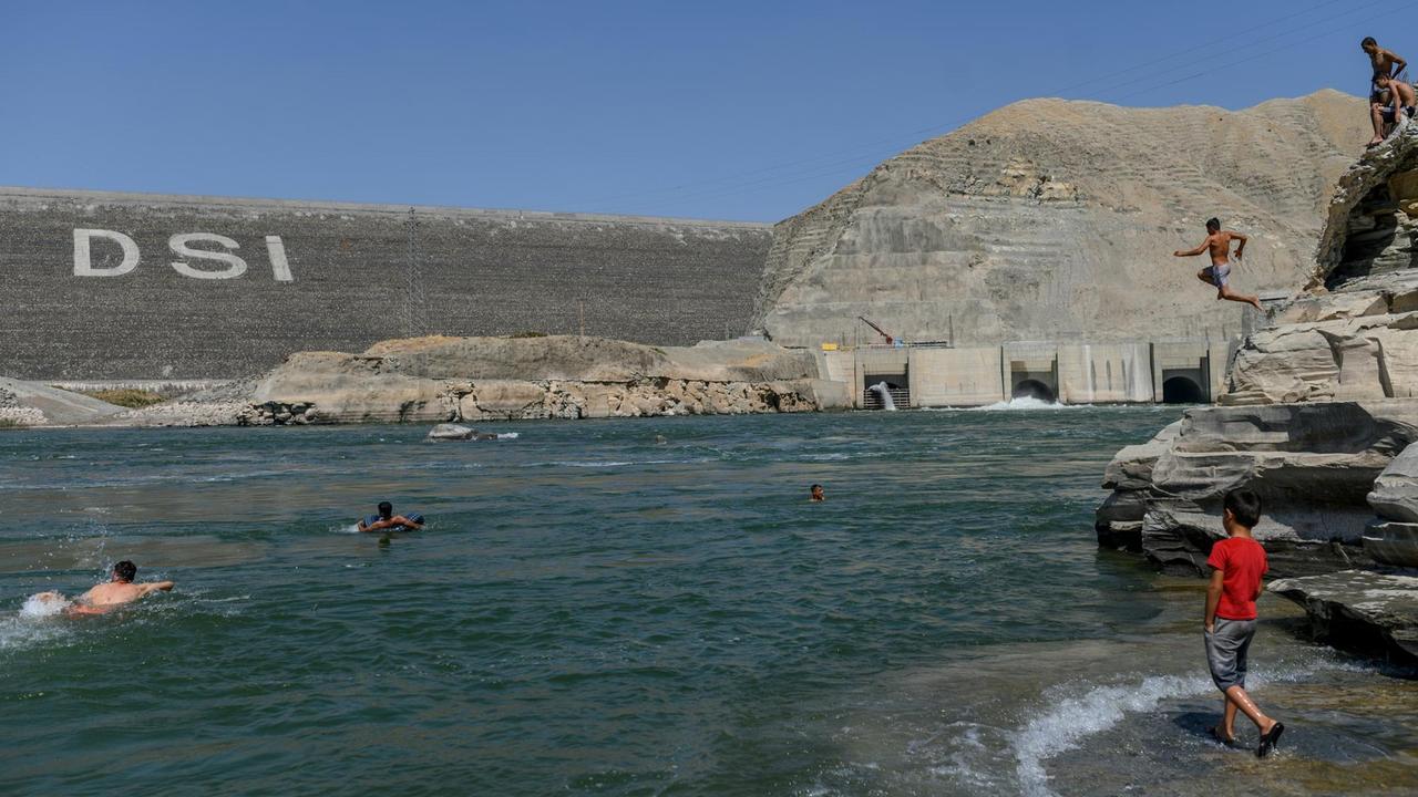 Im Hintergrund ist der Ilisu-Staudamm zu sehen. Im Vordergrund schwimmen junge Männer im Stausee.