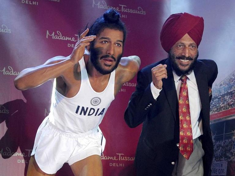 Milkha Singh steht freudig lachend neben seiner Wachsfigur, die ihn als jungen Laufsportler zeigt.