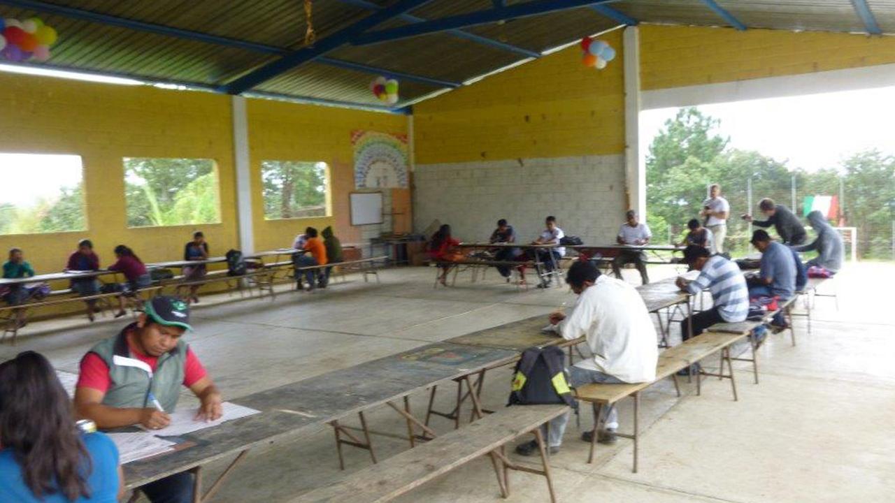 Guatemaltekische Schüler sitzen unter einer Überdachung über Prüfungsaufgaben.