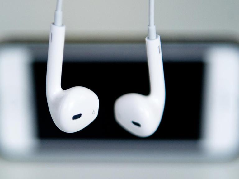 Kopfhörer hängen vor einem Apple Iphone.
