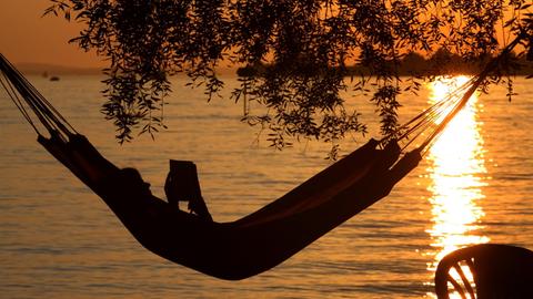 Eine Frau liest in einer Hängematte am Badestrand eines Campingplatzes in Lindau ein Buch.