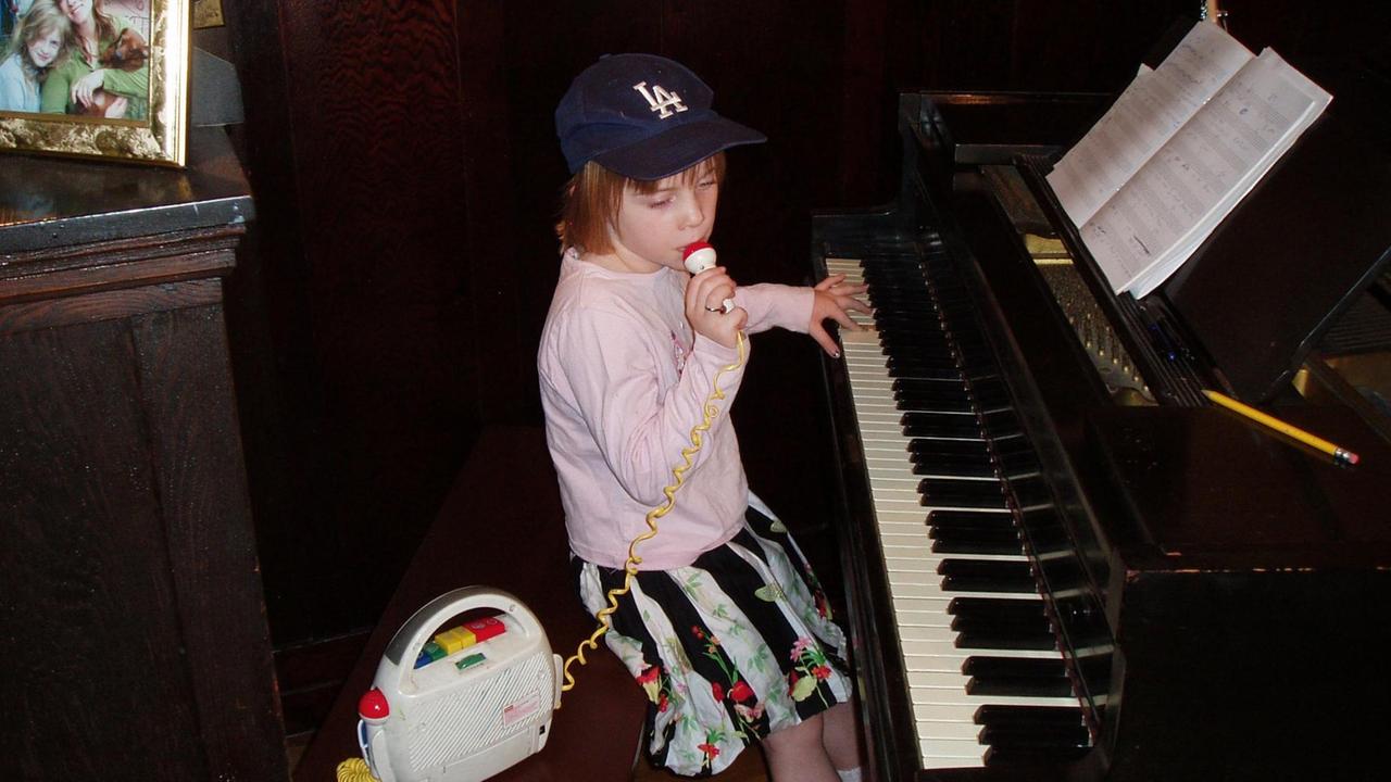 Billie Eilish als Achtjährige, mit einer Hand am Klavier und mit der anderen am Mikrofon eines Kinderrekorders.
