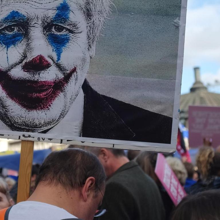 person holding sign with picture of a man wearing clown face art