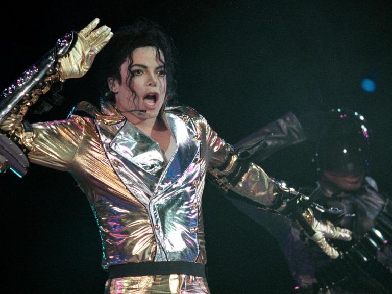 Michael Jackson steht in einem glitzernden Anzug auf der Bühne, tanzt und singt.