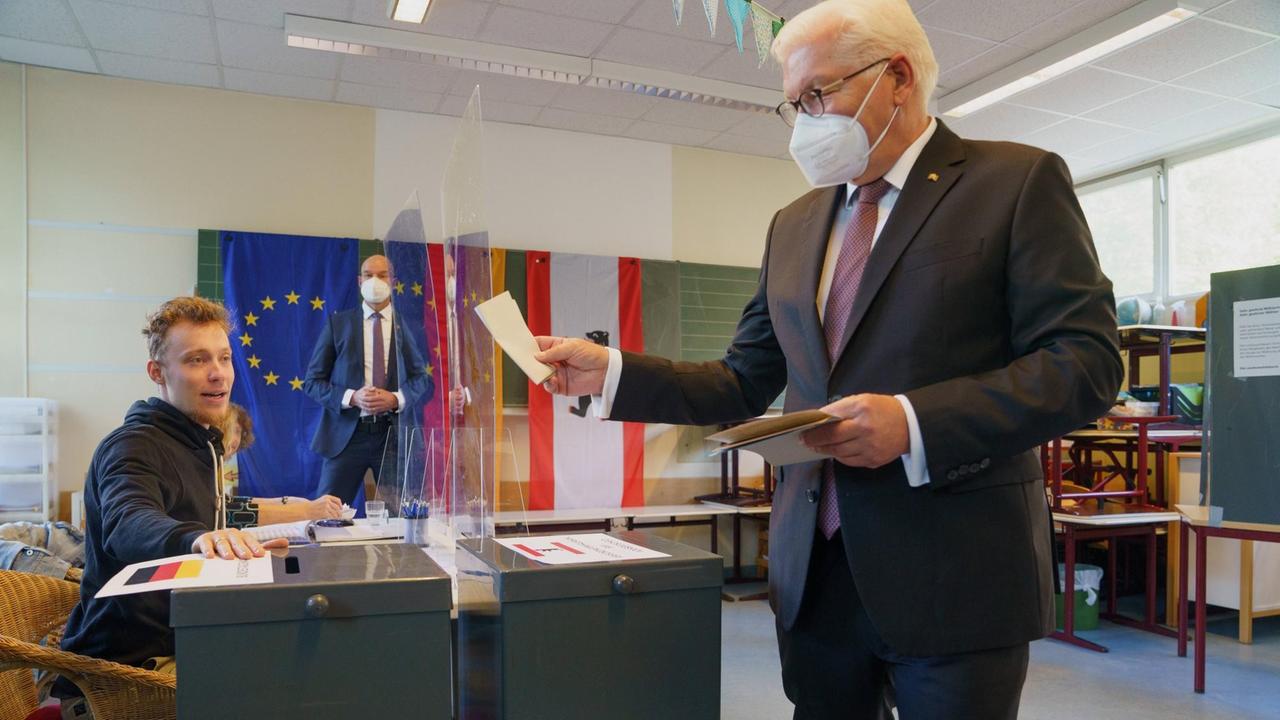 Steinmeier steht mit dem Stimmzettel vor einer Wahlurne, am Tisch sitzt ein Wahlhelfer.