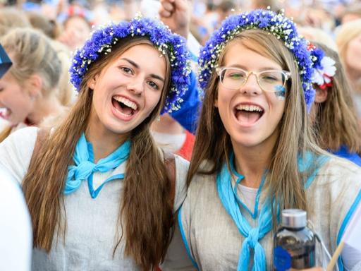 Zwei junge Estinnen mit typischem Blumenkranz und Trachtenbluse singen bei der Großveranstaltung.