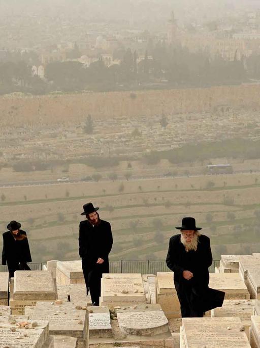 Ultra-orthodoxe Juden auf einem Friedhof auf dem Ölberg in Jerusalem, im Hintergrund der Felsendom.