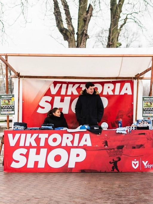 Ein Verkaufsstand mit Fanartikeln von Viktoria 89 vor dem Fußballplatz.