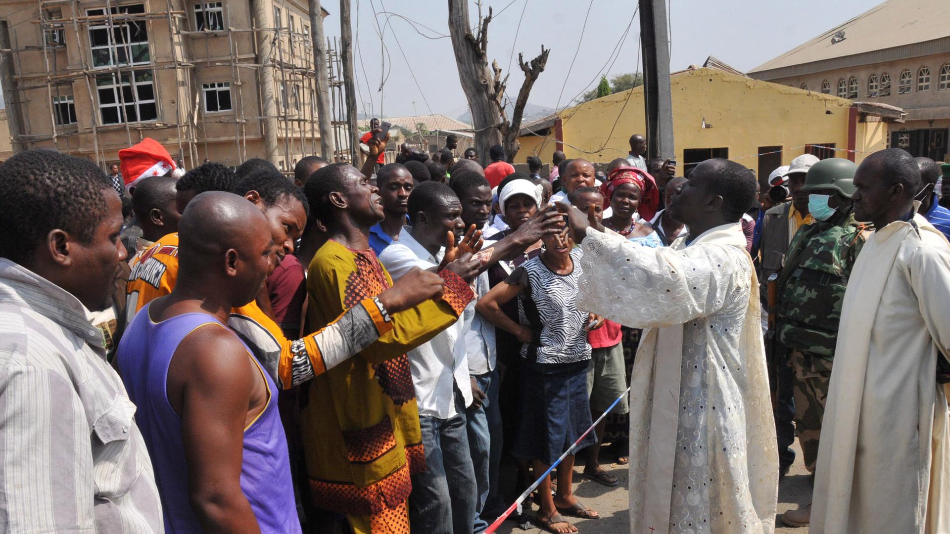 Pfarrer Issac Achi (r) versucht vor der Katholischen Kirche St. Theresa in Madalla (Nigeria) die Menschenmenge zu beruhigen