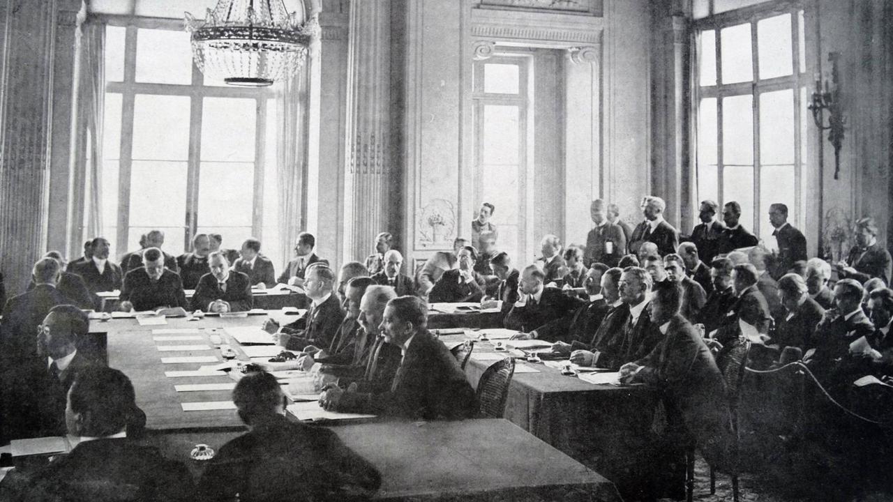 Vertragsverhandlungen in Versailles im Mai 1919. Mehrere Delegationen sitzen in einem großen Saal des Schlosses. 