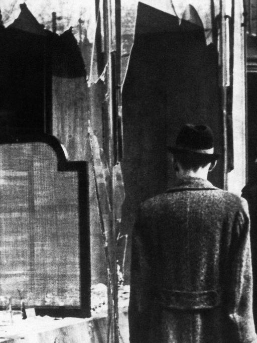 Passanten vor einer zerstörten Fensterfront eines jüdischen Geschäfts in Berlin nach der Reichspogromnacht 1938.
