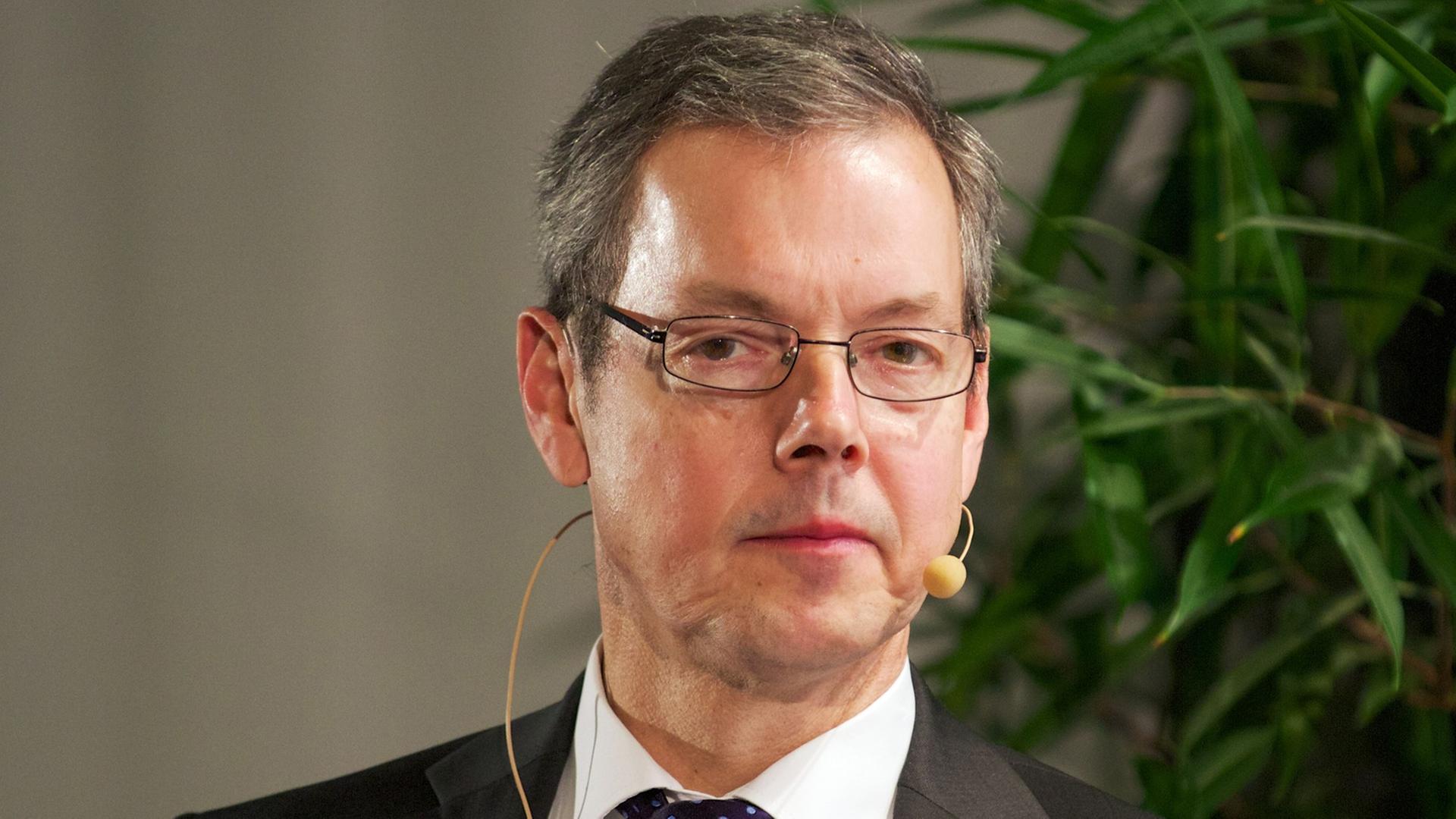 Bofinger blickt mit ernstem Blick in die Kamera. Im Hintergrund sieht man eine grüne Zimmerpflanze.