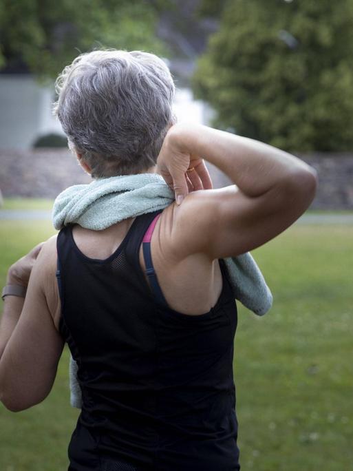 Rückenansicht einer älteren Dame, die von einer Trainerin angeleitet wird. Der Sport findet wegen der Coronakrise und der Ansteckungsgefahr im Freien statt.