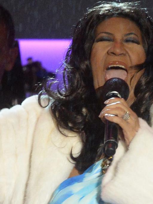 Das BIld zeigt die Sängerin Aretha Franklin beim Singen in einem weißen Pelzmantel.