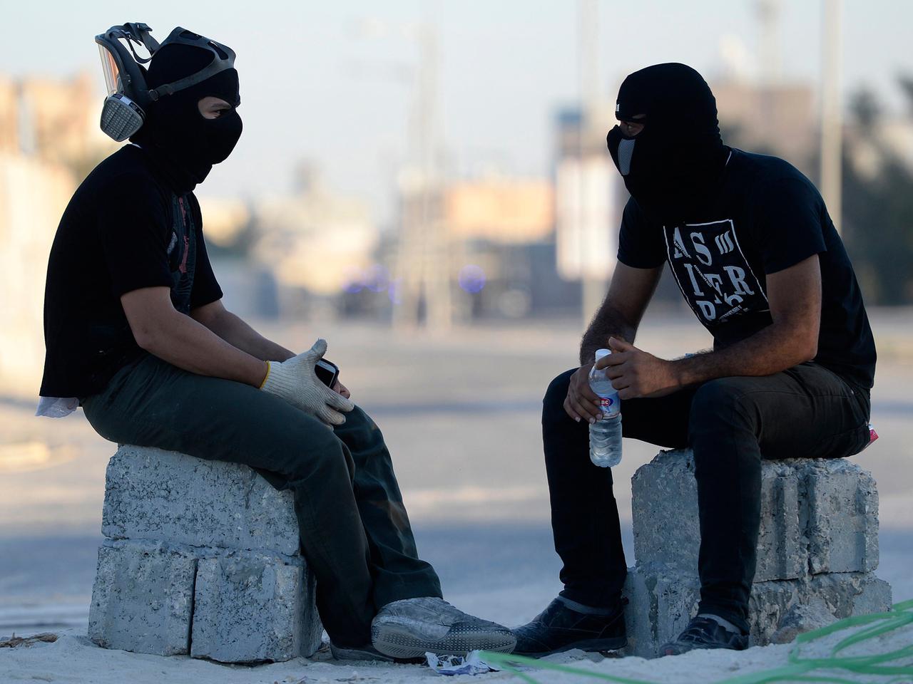 Zwei maskierte Demonstranten sitzen auf großen Steinen und ruhen sich vom Kampf gegen die Polizei aus.