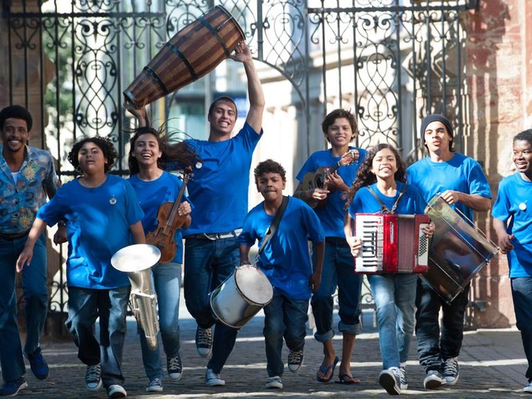 Kinder und Jugendliche laufen in blauen T-Shirts durch ein Tor und halten Musikinstrumente in ihren Händen