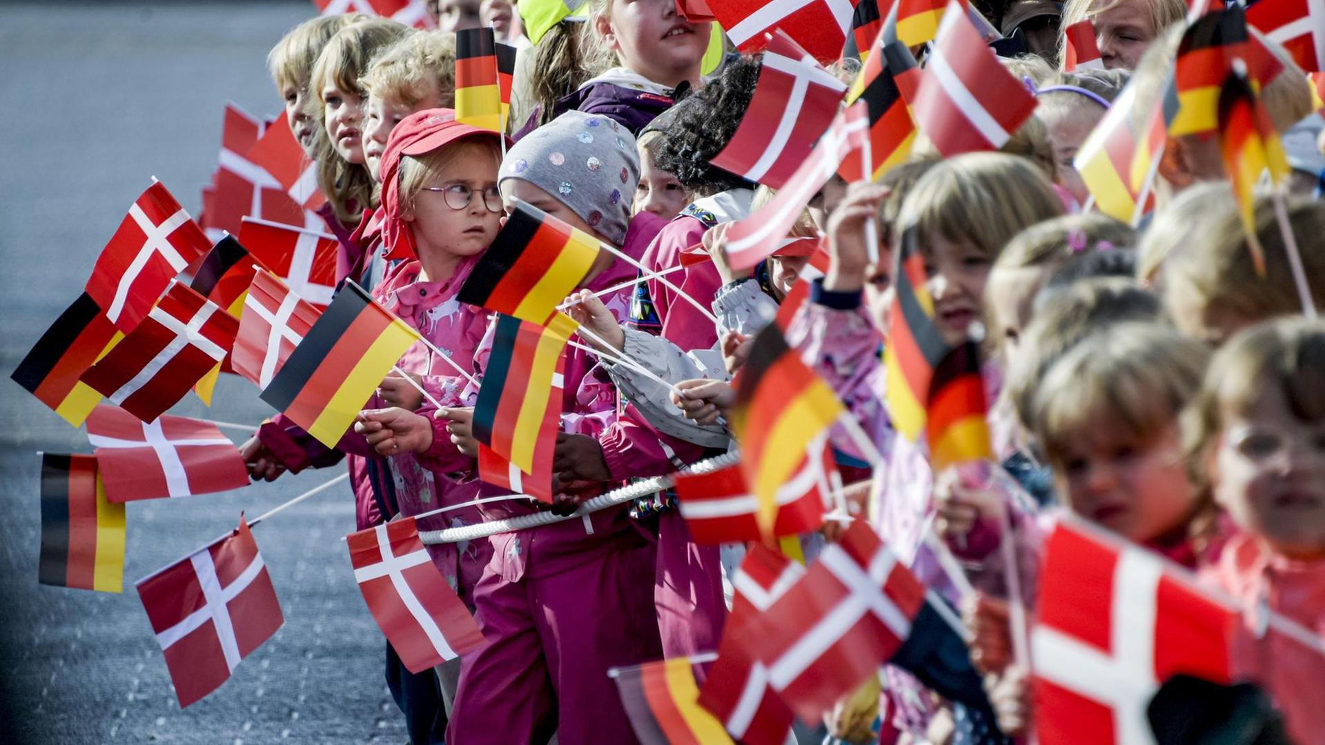 Schulkinder halten kleine deutsche und dänische Fahnen.