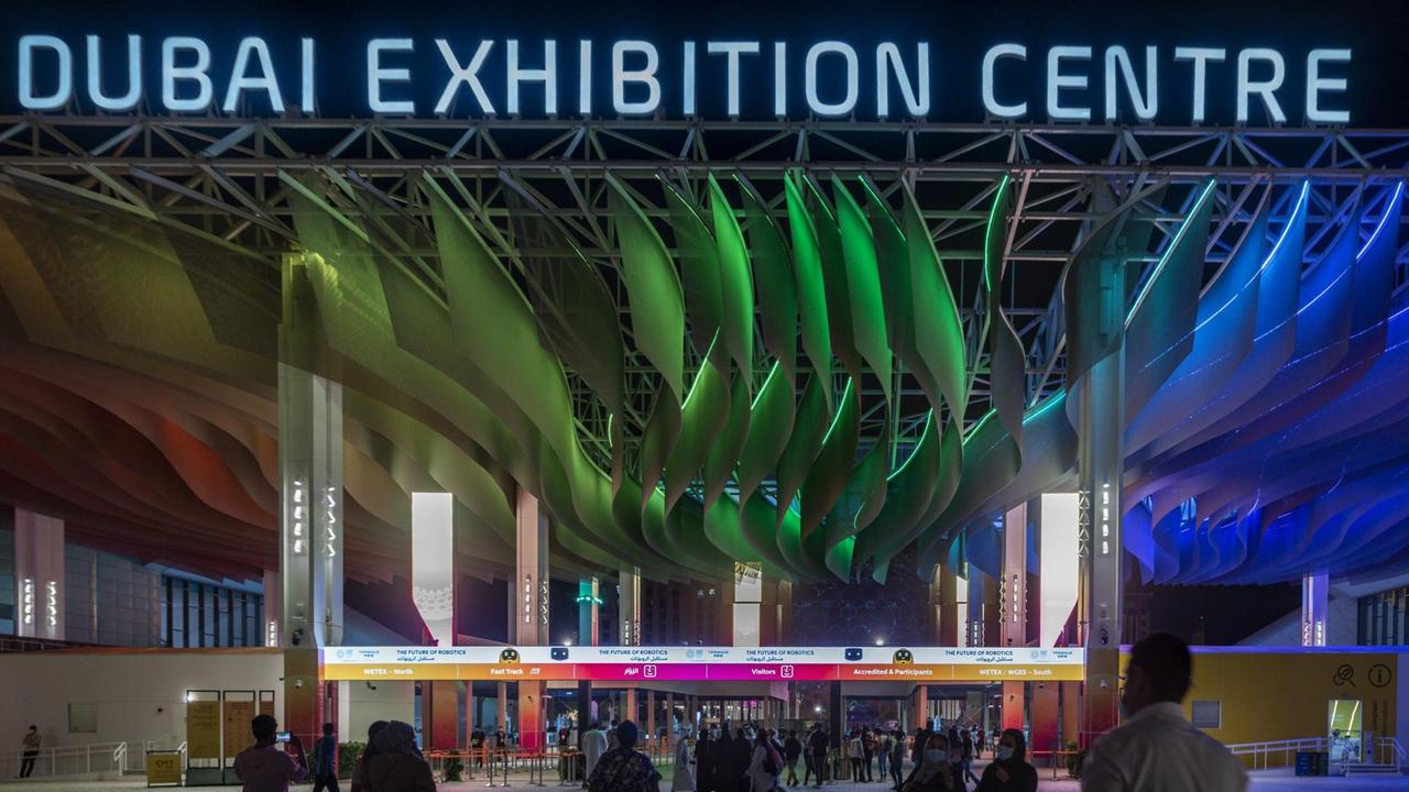 Eingang der Expo 2020 in Dubai bei Dunkelheit: In Neonlicht steht "Dubai Exhibition Center" über dem Eingang.