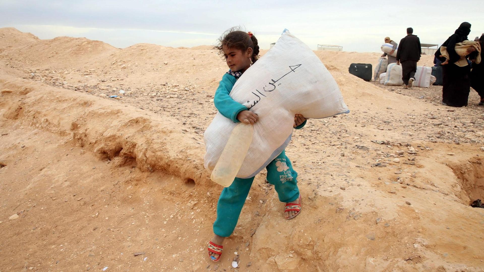 Ein syrisches Flüchtlingsmädchen trägt einen Getreidesack auf dem Weg in ein Flüchtlingscamp auf der jordanischen Seite an der Grenze zu Syrien.