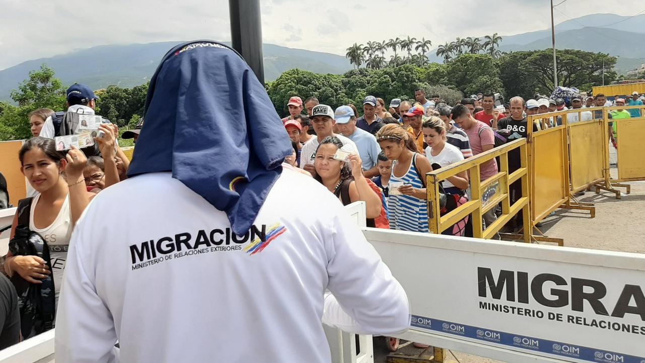 Ein Kontrolleur der Migrationsbehörde mit Sonnenschutz kontrolliert die Venezolaner, die ihre Dokumente hochhalten.