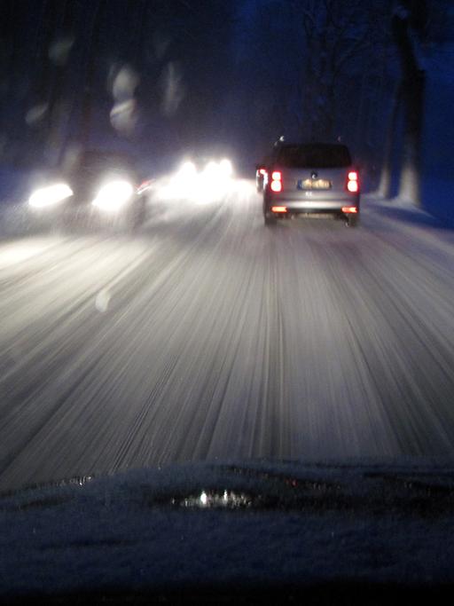 Blick durch eine Autoscheibe auf eine schneeglatte Straße im Dunkeln.