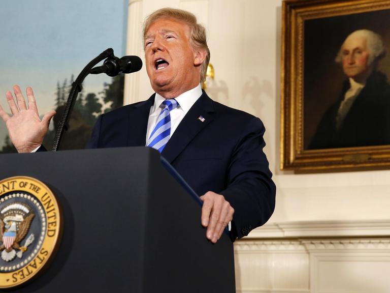 Präsident Donald Trump steht an einem Rednerpult. Die rechte Hand ist erhoben. Er verkündet das Ende des Atom-Deals mit dem Iran. Im Hintergrund ist ein Gemälde von George Washington zu sehen.