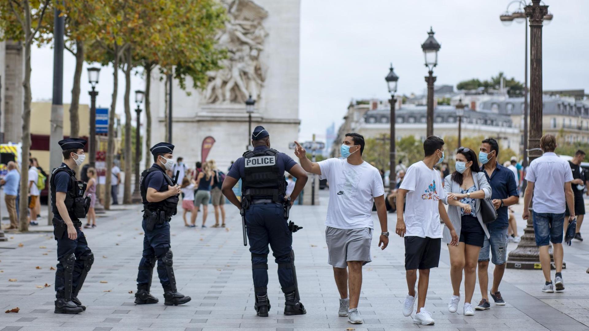 Paris: Touristen mit Schutzmasken gehen auf der Prachtstraße Champs-Elysees an Polizisten vorbei.