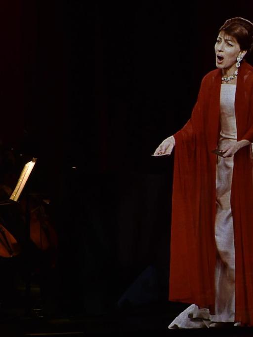 Ein dreidimensionales Hologramm, das aussieht wie die Opernsängerin Maria Callas steht vor einem Orchester und singt.