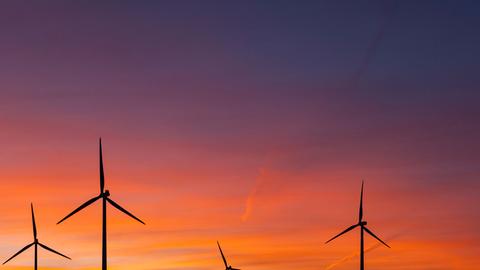 Windräder stehen auf einem Feld bei Wormlage in der brandenburgischen Lausitz vor dem vom Sonnenuntergang rot gefärbten Abendhimmel.