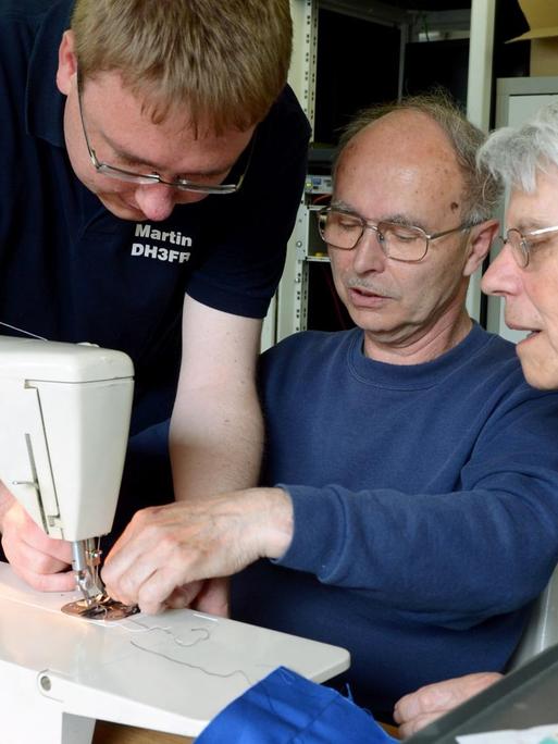 Der Diplom-Ingenieur und leidenschaftliche Bastler Martin Kramer (l) repariert im Repair-Café zusammen mit Johann Schütt (M) eine Nähmaschine von Wolfgang Rogoll.