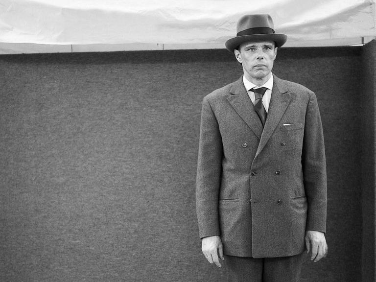 Joseph Beuys steht regunglos, mit Hut auf dem Kopf, vor einer Filzwand auf der 4. documenta in Kassel, 1968.