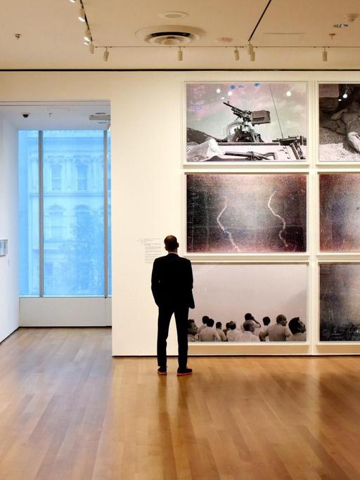 Ein Mann steht in einem Ausstellungsraum vor einer Wand und schaut sich Fotografien an.