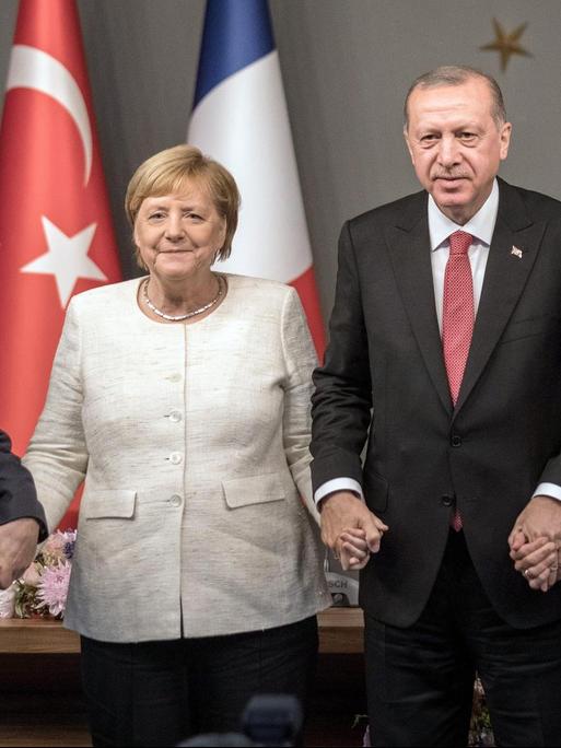 Wladimir Putin, Bundeskanzlerin Angela Merkel (CDU), Recep Tayyip Erdogan, Staatspräsident der Türkei, und Emmanuel Macron, Präsident von Frankreich, reichen sich bei einer Pressekonferenz nach dem Gipfeltreffen die Hände.