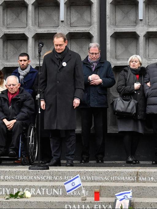 Berlins regierender Bürgermeister Müller steht mit gesenktem Kopf gemeinsam mit weiteren Menschen auf den Stufen, in die die Namen der Terroropfer eingefasst sind.