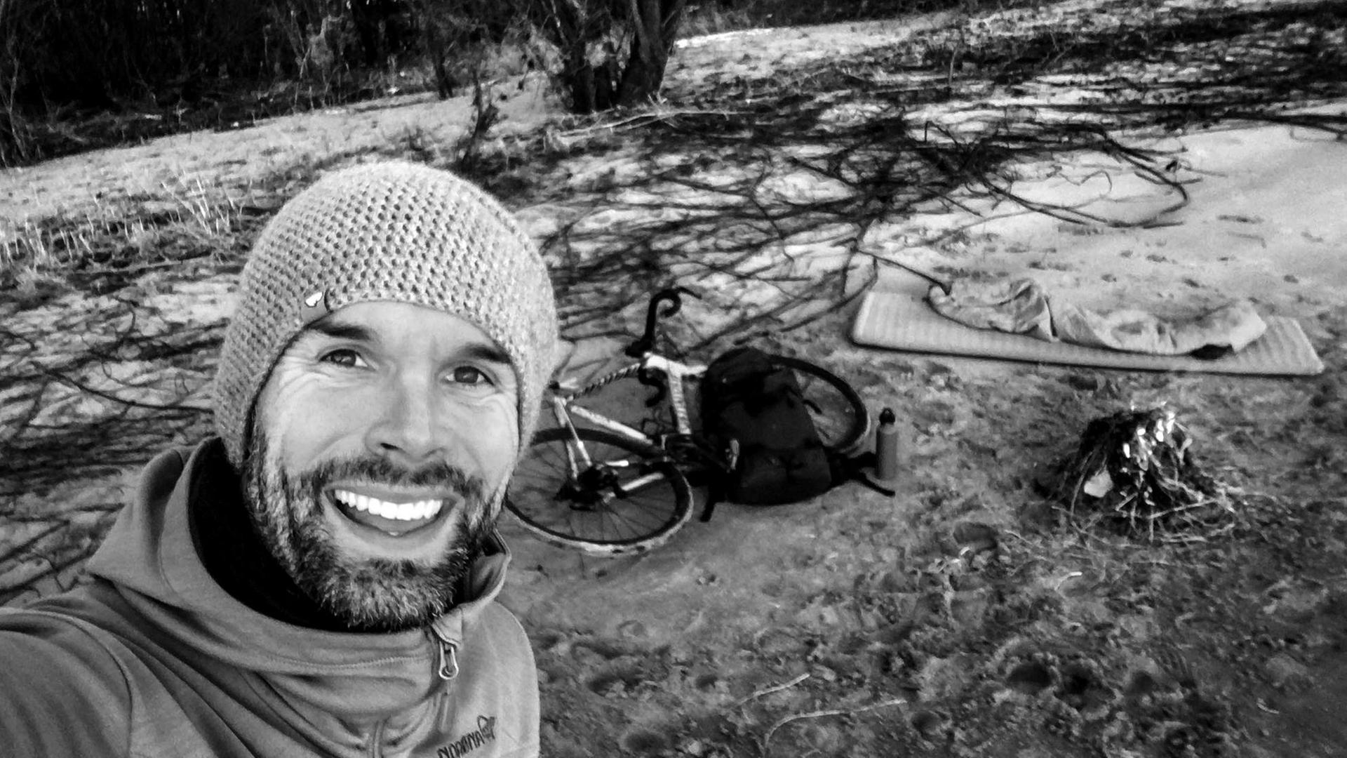 Buchautor Christo Foerster lacht in die Kamera, im Hintergrund sieht man sein improvisiertes Bett in freier Natur