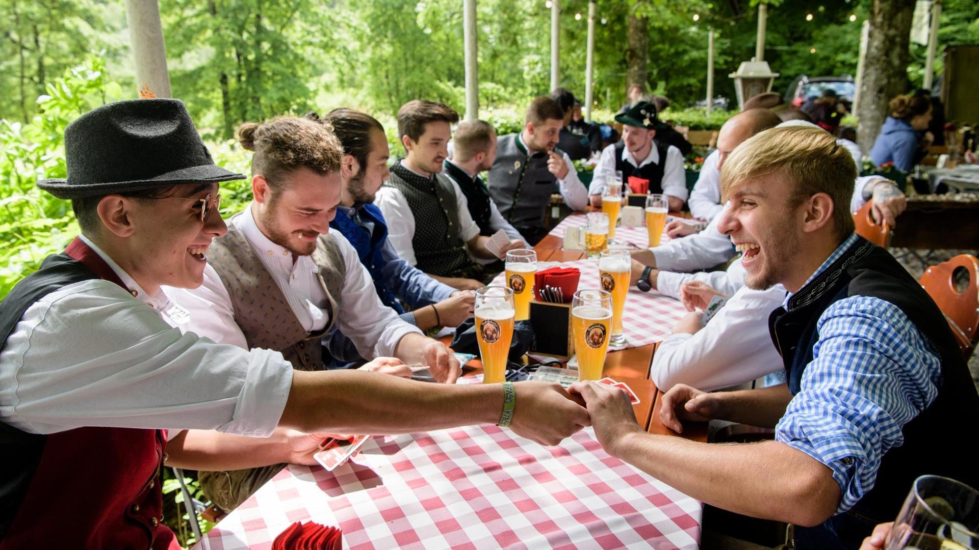 Eine Männergruppe spielt im Biergarten eines Wirtshauses an der Isar ein Kartenspiel.