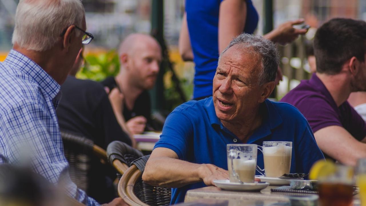 Zwei Männer sitzen in einem Straßencafé und trinken Milchkaffee.