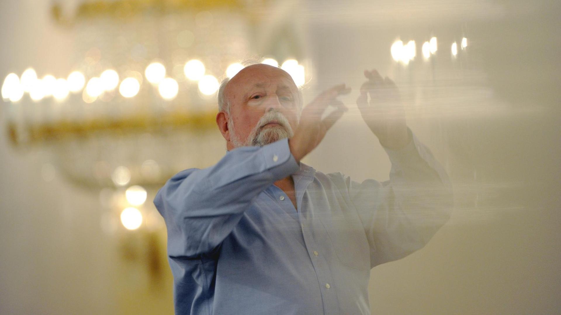 Krzysztof Penderecki steht in einem hell erleuchteten Saal und dirigiert.