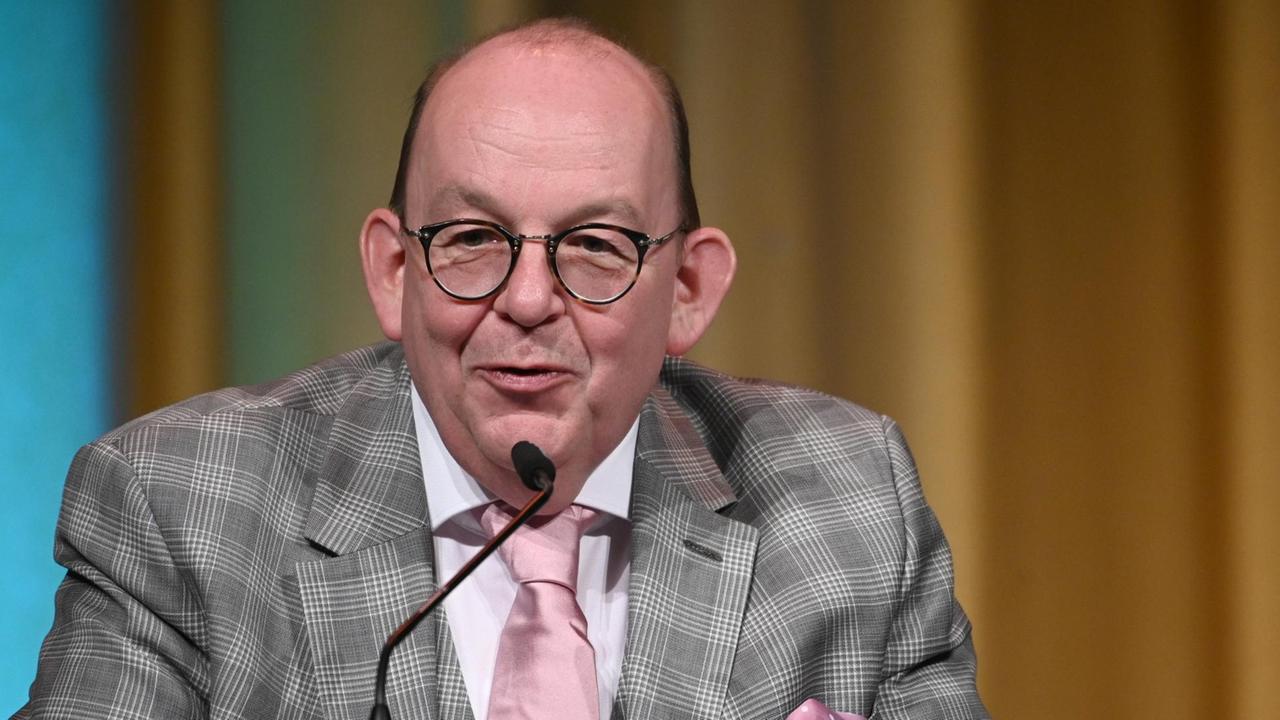 Denis Scheck mit kariertem Jackett und rosa Krawatte lächend an einem Mikrofon.