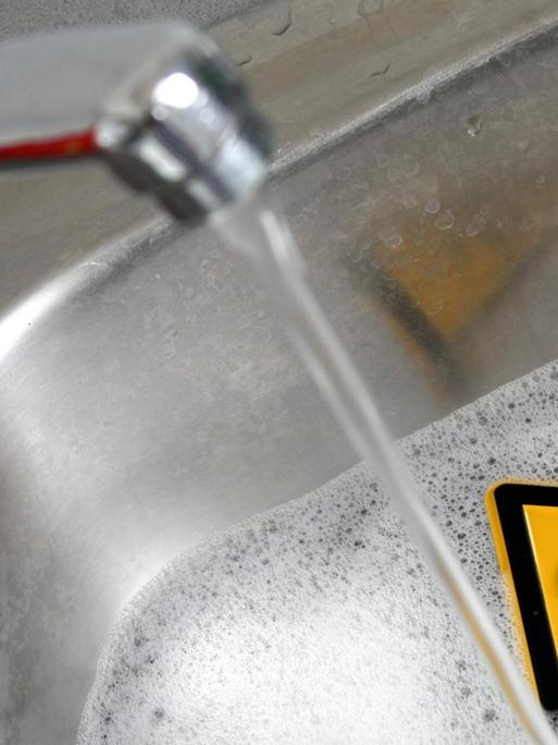 Symbolbild für Gefahren im Haushalt: Warnschild Achtung Gift in einer mit Wasser und Reinigungsmittel gefüllten Spüle in der Küche sowie Wasserhahn