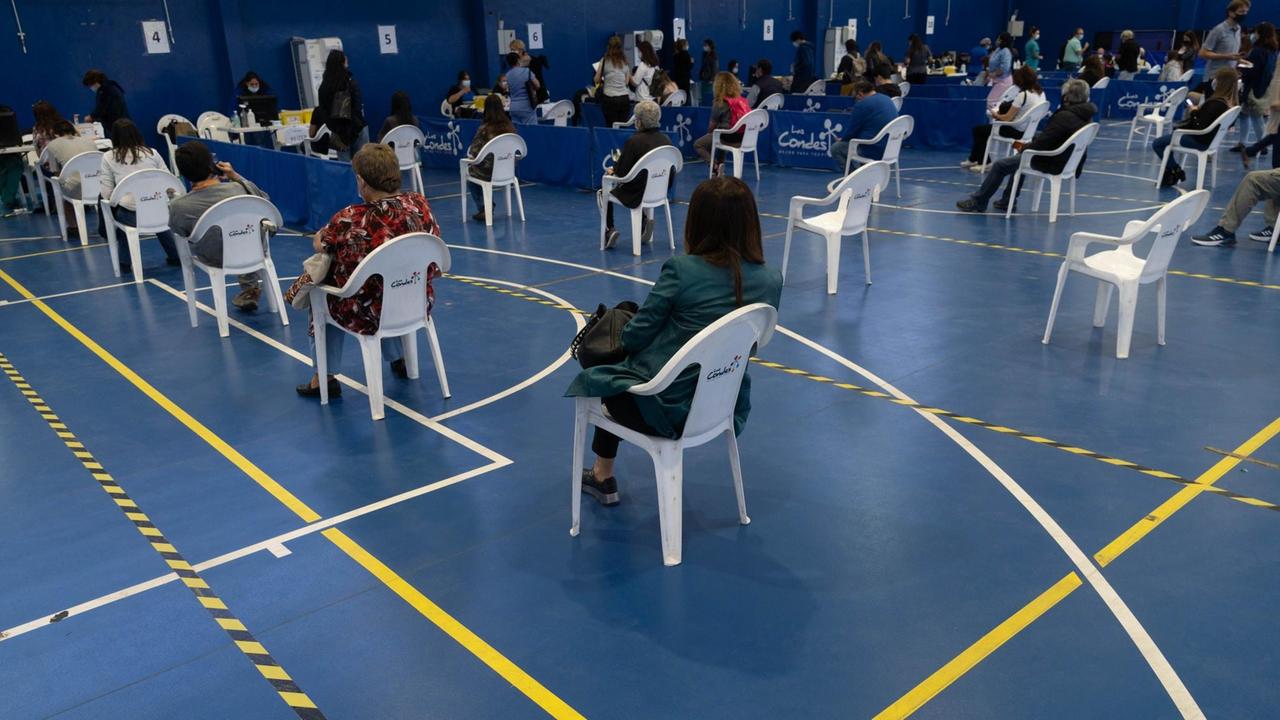In einer Turnhalle in Santiago de Chile, die zu einem Impfzentrum umfunktioniert wurde, warten im März 2021 Menschen in Plastikstühlen auf die Impfung mit Sinovac oder Pfizer.
