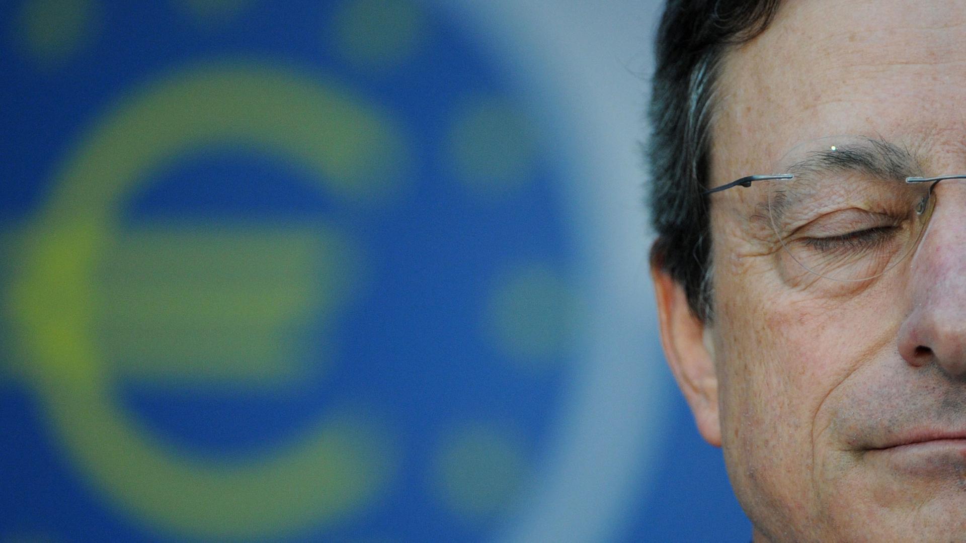 Mario Draghi hat die Augen geschlossen, im Hintergrund ist ein Eurozeichen zu sehen.