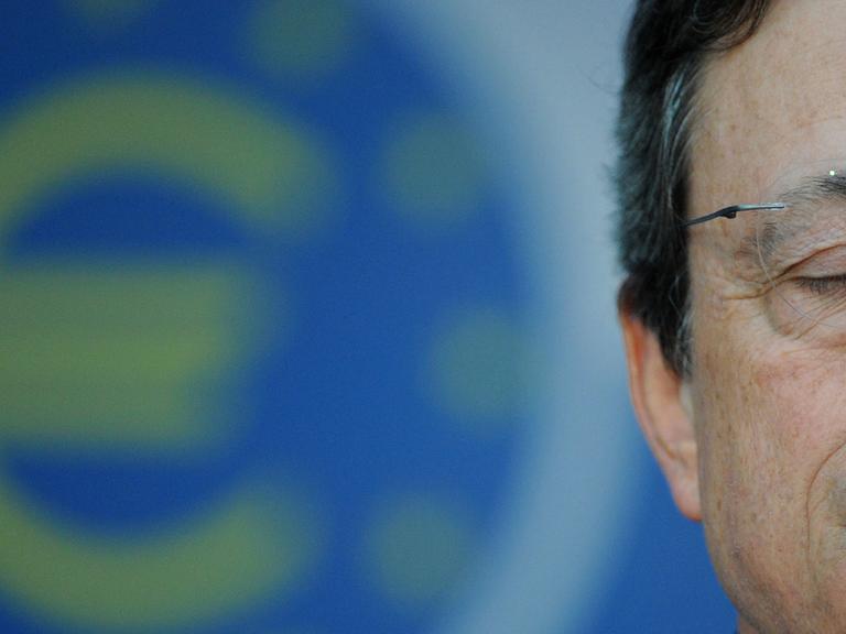 Mario Draghi hat die Augen geschlossen, im Hintergrund ist ein Eurozeichen zu sehen.