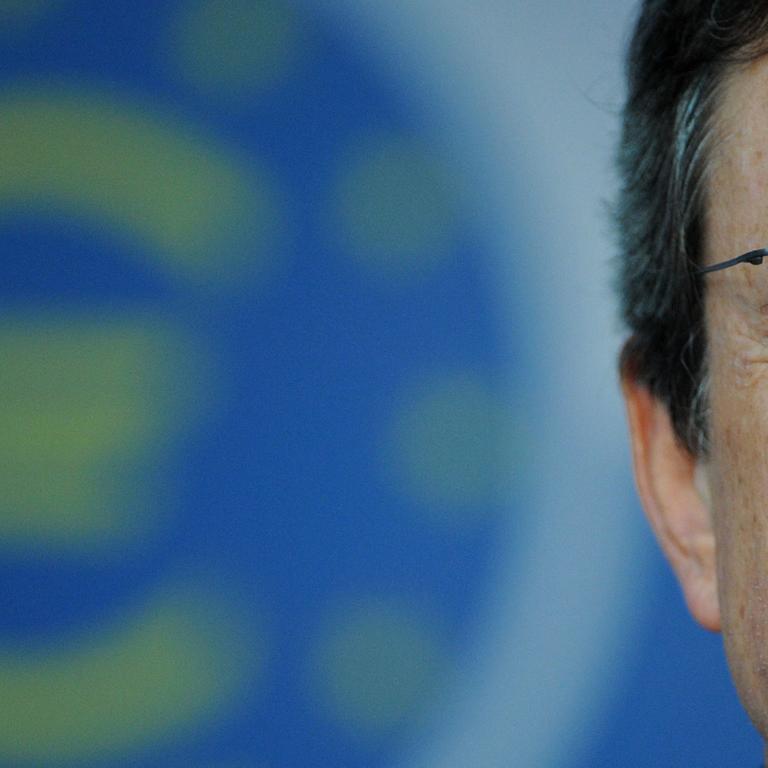 Mario Draghi hat die Augen geschlossen, im Hintergrund ist ein Eurozeichen zu sehen.