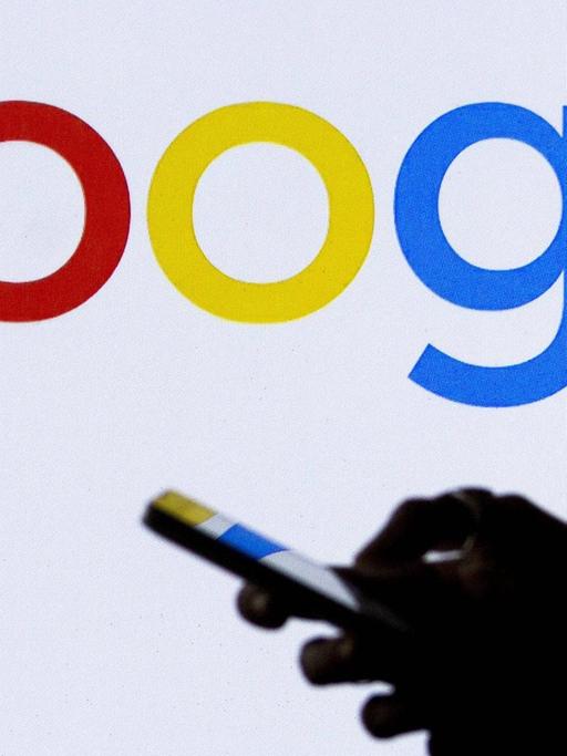 Hand mit Smartphone vor dem Logo von Google