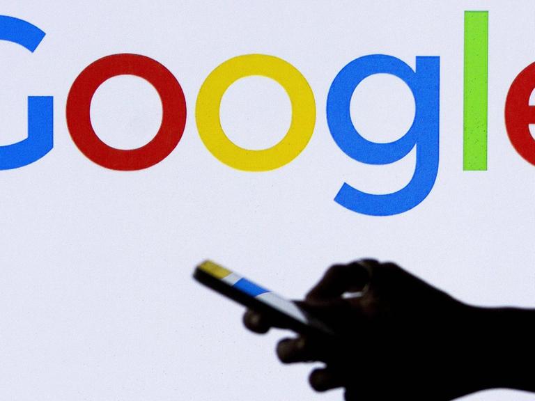 Hand mit Smartphone vor dem Logo von Google