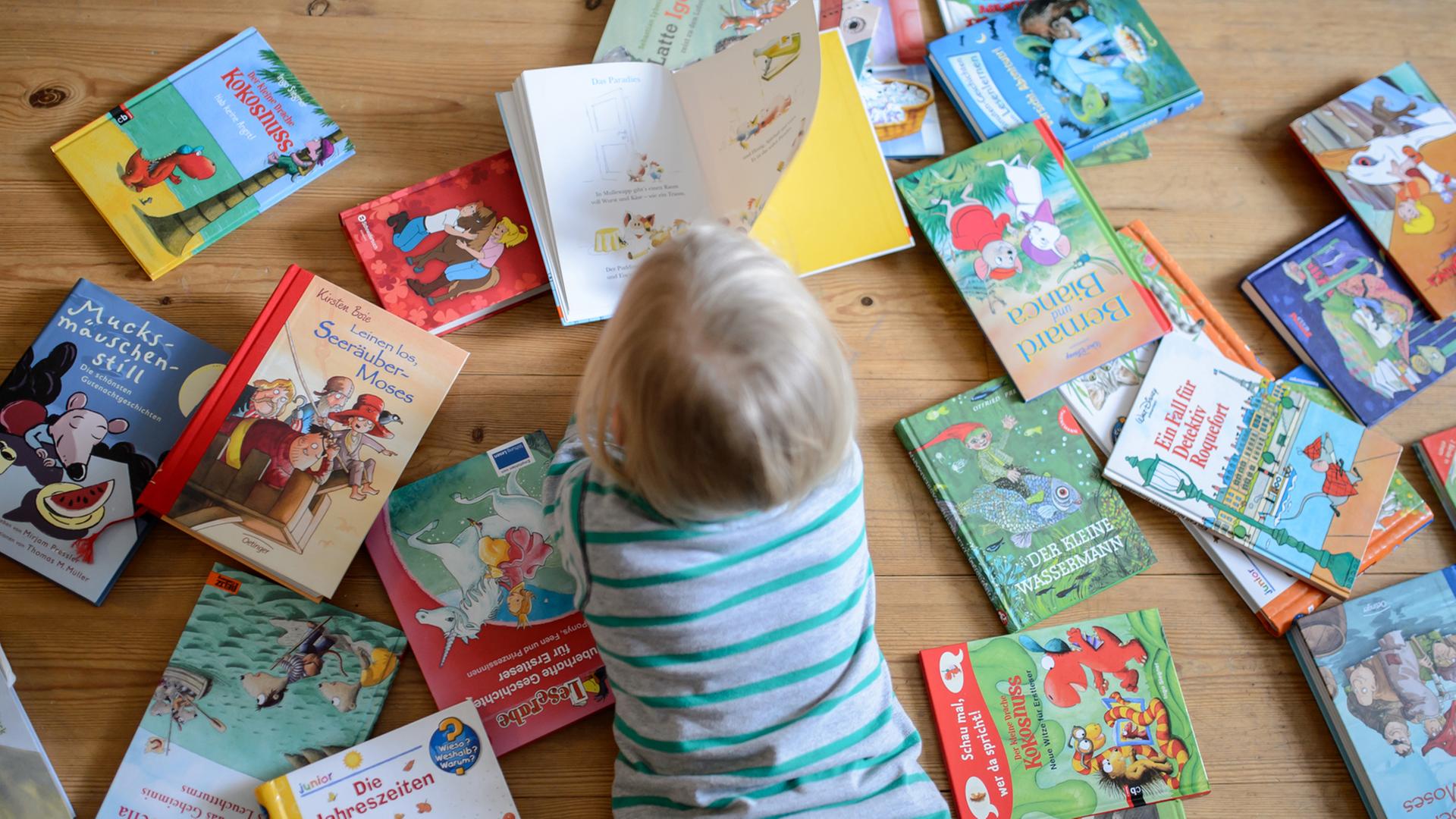 Ein Kind liegt zwischen vielen Büchern und schaut sich ein Buch an, aufgenommen am 28.01.2015 in Dresden (Sachsen).