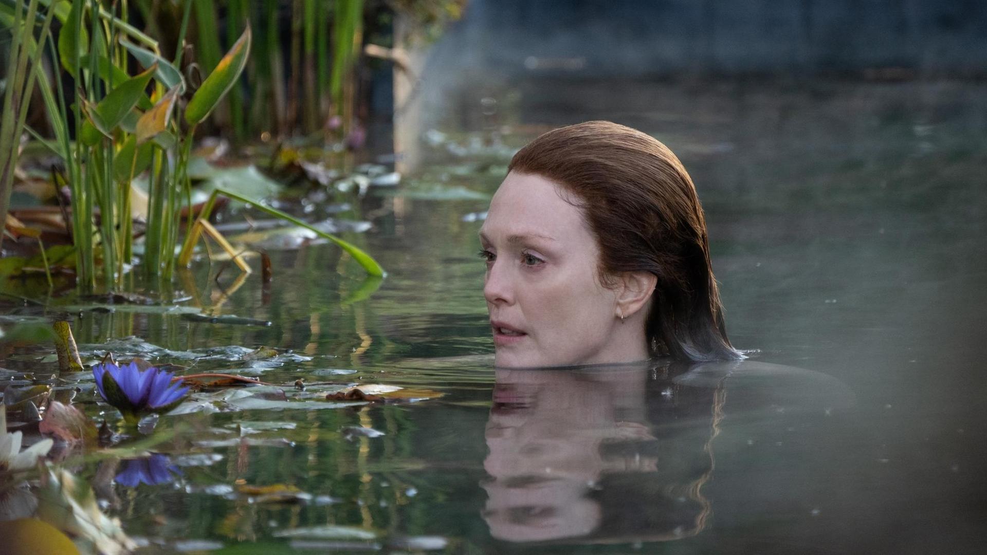 Die Schauspielerin Julianne Moore schwimmt im nebligen Wasser neben Schilf und Seerosen.